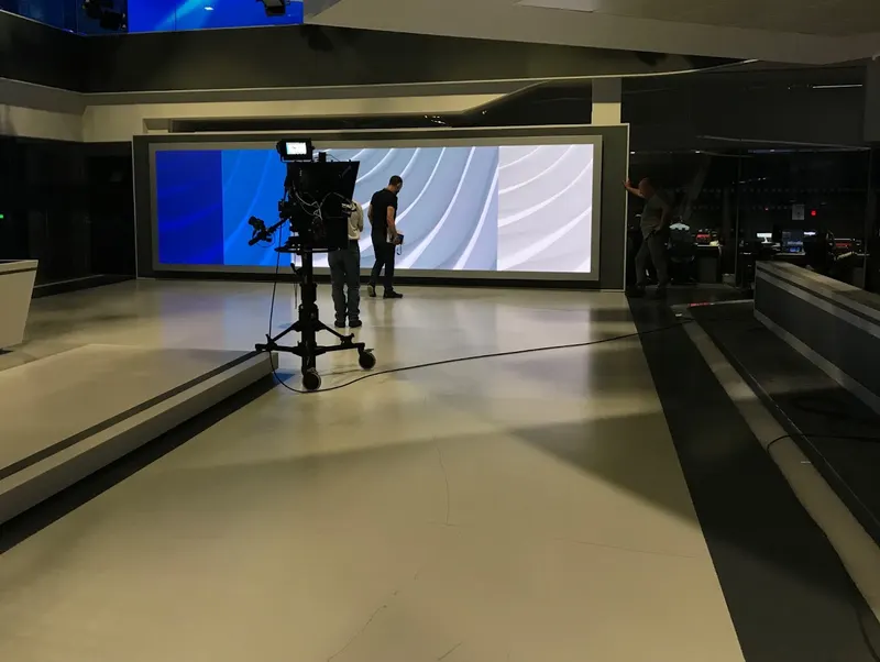 An engineer inspecting the wide LED video wall in Al Araby TV's Park Royal studio, with a pedestal camera in the foreground.