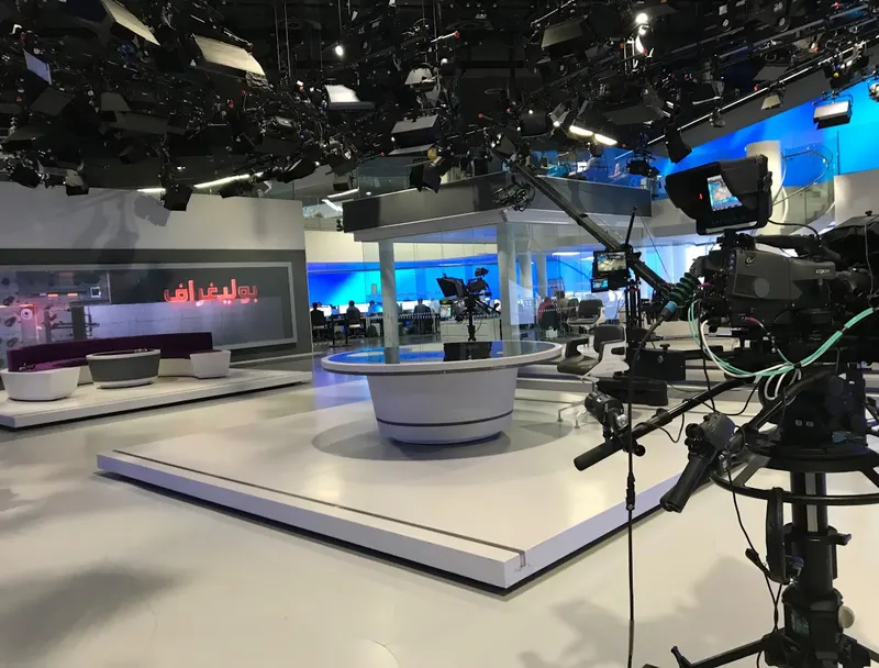 Al Araby TV's studio floor, with a round presenter desk, a sofa area, a camera jib and the newsroom visible behind.