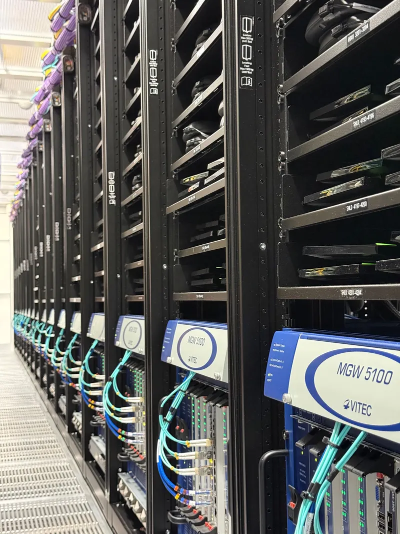 A row of racks in the Prime Video device-farm data hall, with shelves of test devices above VITEC MGW 5100 encoders and fibre patching.