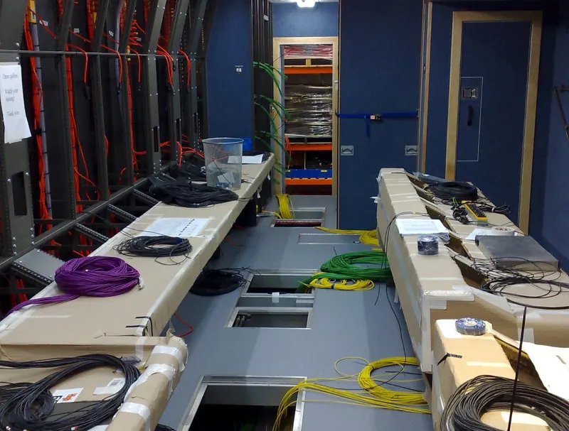 The aisle of an O21 Television OB truck during fit-out, with floor hatches open and coils of cable laid out on the protected desks.