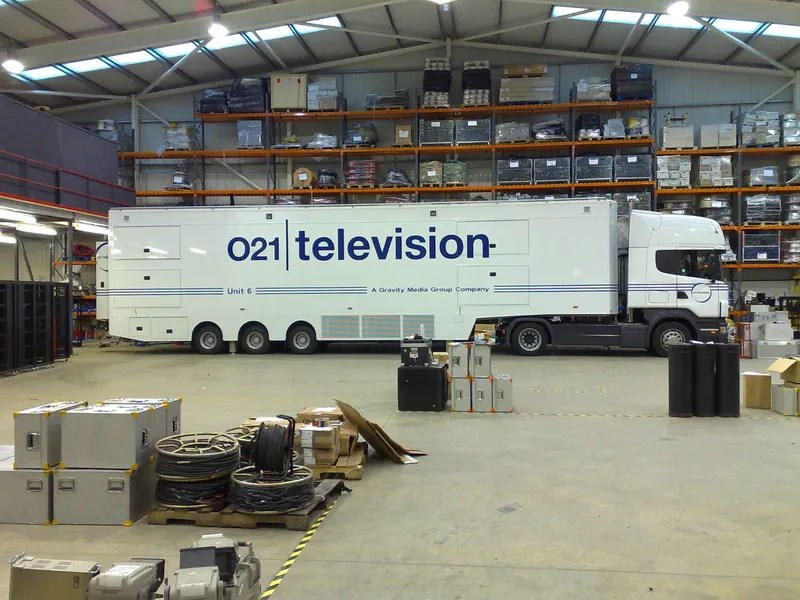 O21 Television's Unit 6 outside broadcast truck parked in a warehouse, surrounded by flight cases and cable drums.
