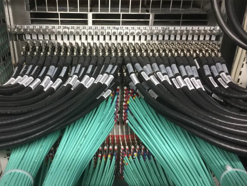 A 32-way coaxial panel in IMG's Stockley Park data centre, with labelled black coax cables above and teal cable looms fanning out below.